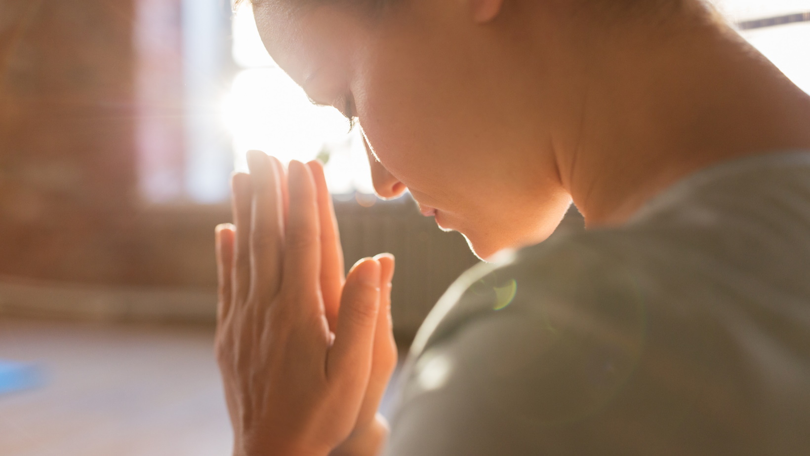 Eine Frau in einer meditativen Haltung mit geschlossenen Augen vor einem hellen und geräumigen Yogastudio in Tetyana Shenk Ayurveda Well-Being Praxis